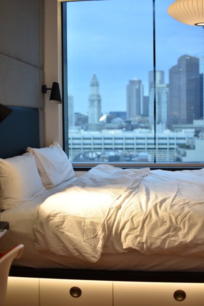 Modern hotel room overlooking Boston skyline, featuring luxury bedding.