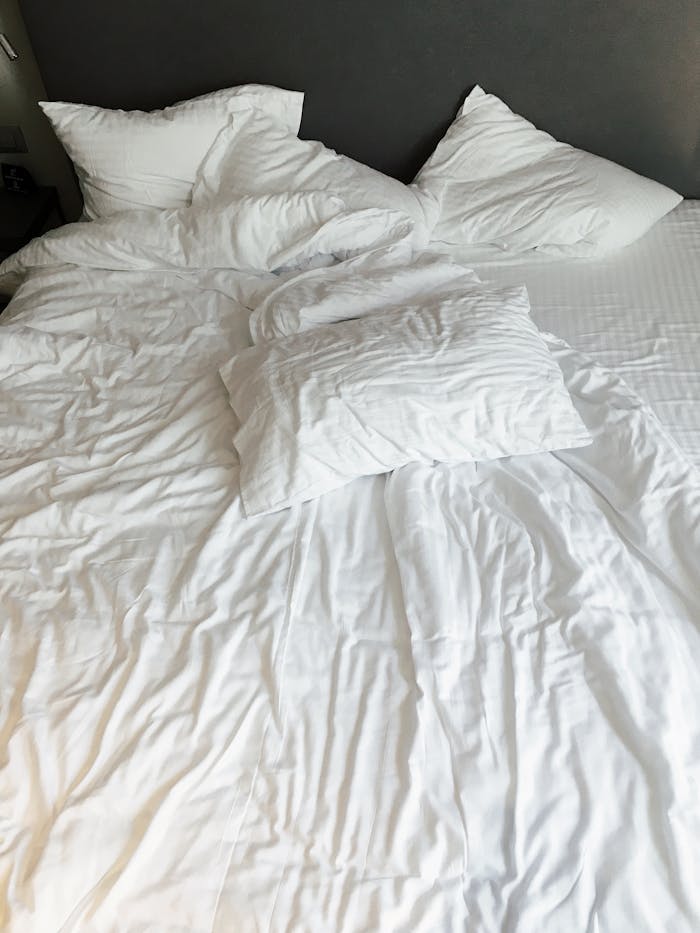 An inviting unmade bed with white linens and pillows in a modern bedroom setting.