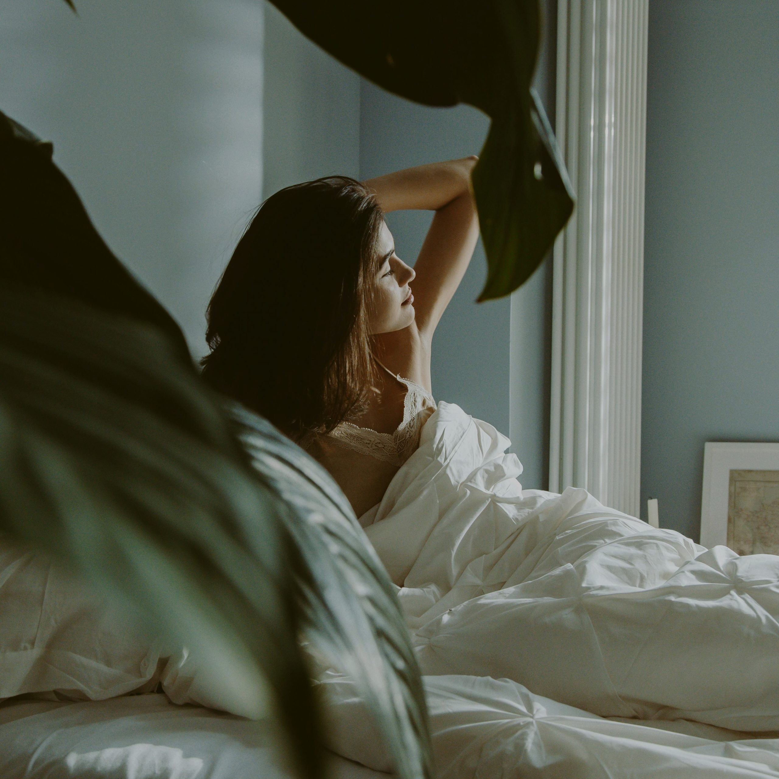 Woman sitting in bed, bathed in morning sunlight, looking refreshed and energized after a good night's sleep.